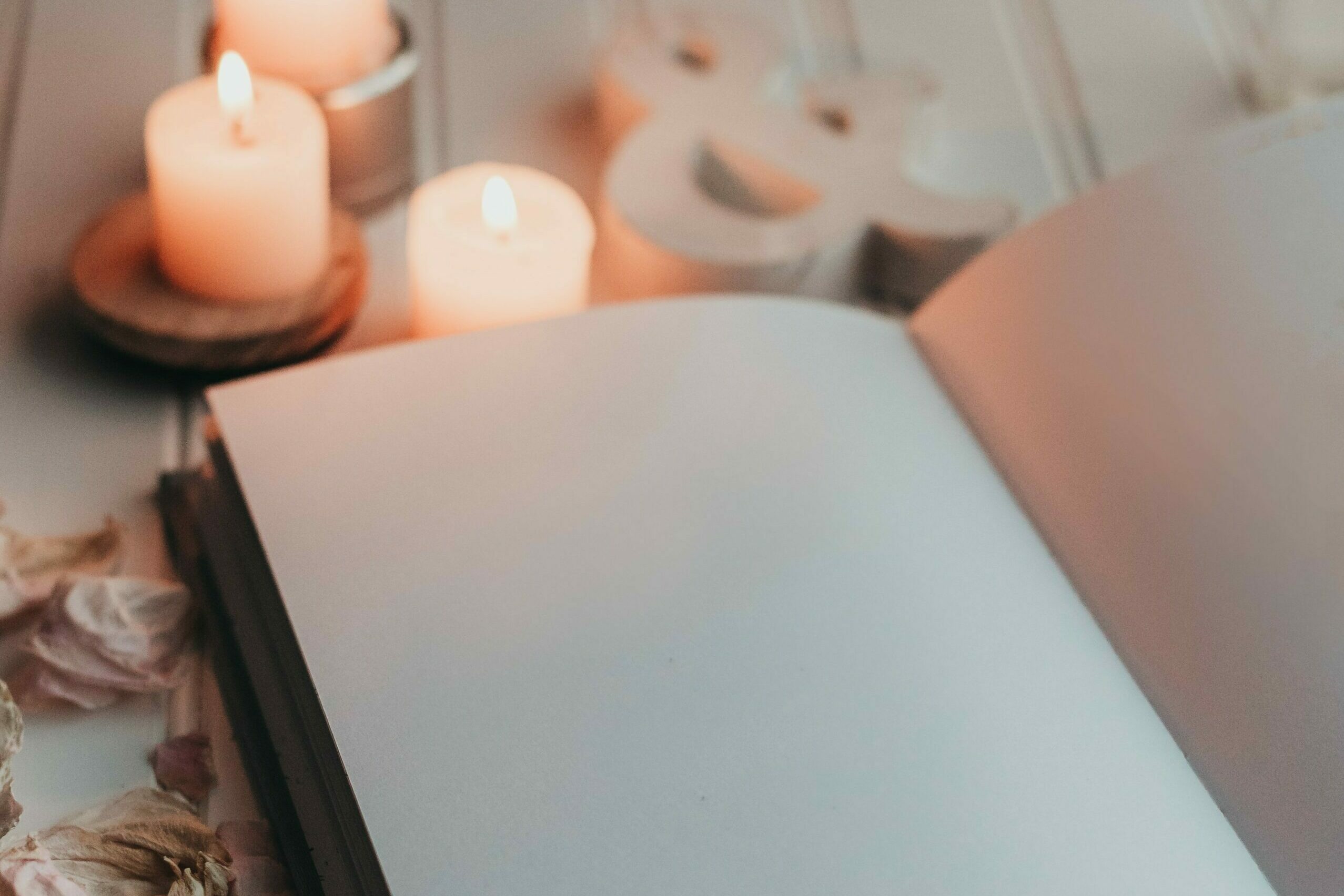 Cahier ouvert sur une page blanche, posé sur une table en bois blanc, devant 3 bougies blanches allumées et une sculpture en bois d'esperluette. Venez découvrir l'histoire de Symphonie Feng Shui