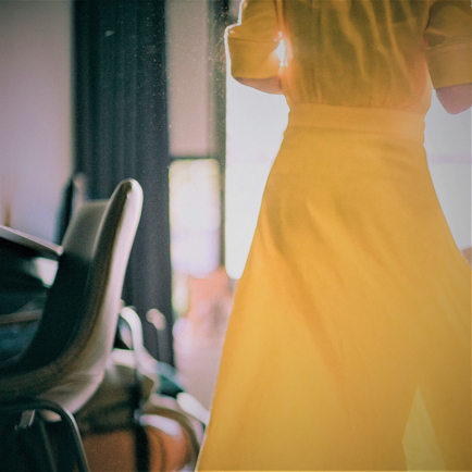 Jeune femme portant une robe jaune à l'intérieur sur un fond de rayons de soleil.